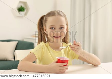 Cute Little Girl With Tasty Yogurt At White Table At Home