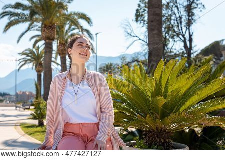 Young Happy Smiling Caucasian Woman Sitting On Beanch In Background With Palms. Summer And Vacation.