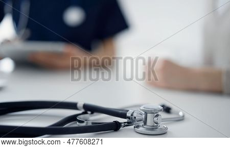 Stethoscope Lying On The Tablet Computer In Front Of A Doctor And Patient At The Background. Medicin