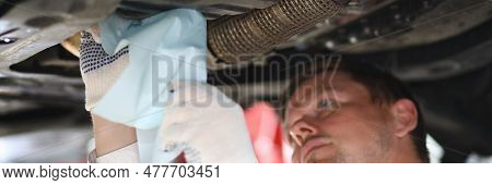Auto Mechanic Inspects Car Leak And Suspension Parts Of Raised Car With Napkin At Repair Station. Se