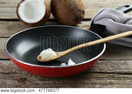 Frying Pan With Organic Coconut Cooking Oil And Spoon On Wooden Table, Closeup