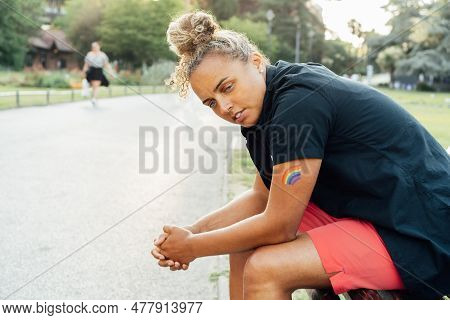 Sad Frustrated Lesbian Woman With Lgbtq Rainbow Tattoo On Her Hand Sitting On The Park Bench Alone. 
