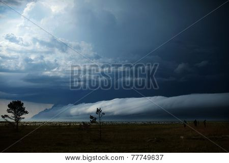 three people look at the looming clouds over the sea during a storm