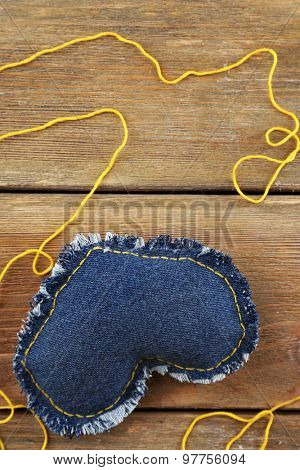 Denim heart and thread on wooden background