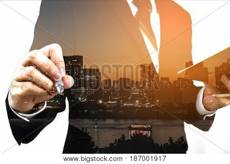 Businessman holding memo and prompt to write down. Double exposure, panoramic view contemporary megalopolis background, orange sun light