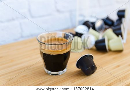 Close up of tasty espresso with foam and coffee capsules on wooden background.Copy space.