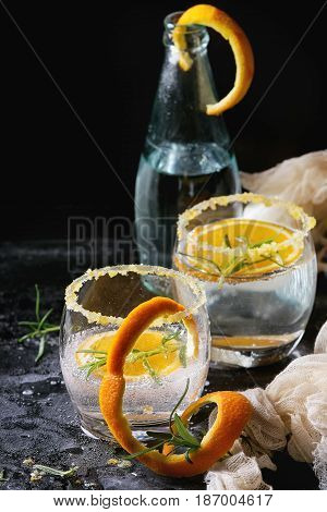 Tonic water cocktail with rosemary and orange. Two glasses and bottle with zest sugar and bubbles with textile gauze over black texture background. Refreshing beverage alco non alcohol