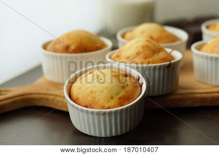 Homemade vanilla muffins in porcelain forms on a wooden board