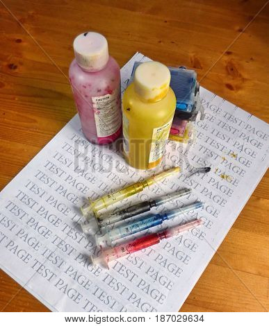 Set of Ink cartridges, refill paints in bottles and dirty syringes. On printed test page. Jet printer maintenance.