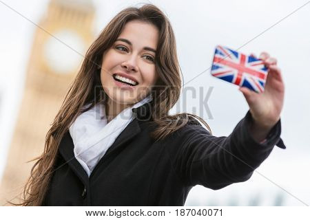 Girl or young woman tourist on vacation taking a selfie photograph by Big Ben with Union Jack cell phone, London, England, Great Britain