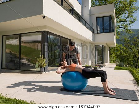 young beautiful woman and personal trainer doing exercise with pilates ball in front of her luxury home
