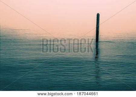Calm water with solitary wooden post and reflection. Simple serene image with connotations of Zen Buddhism.