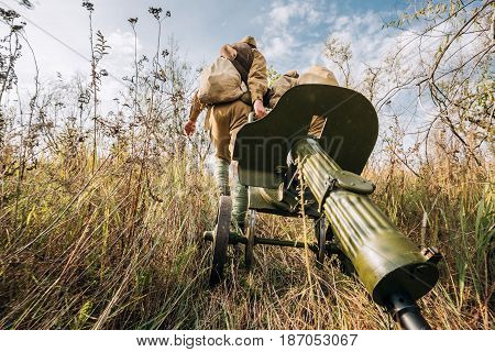 Two Reenactors Dressed As Russian Soviet Red Army Soldiers Of World War II Walking With With Maxim's Machine Gun Weapon In Autumn Meadow