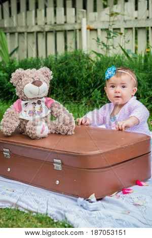 Baby sitting near suitcase in the summer garden