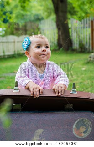 Baby sitting near suitcase in the summer garden