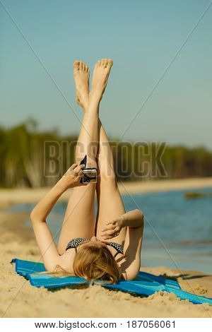 Summertime pleasures enjoying vacation concept. Woman in bikini sunbathing and relaxing on beach using smartphone checking social media and writing sms