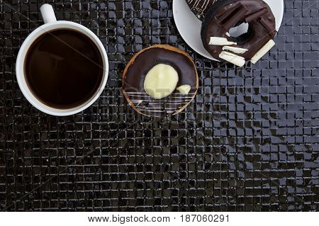 Chocolate donut with cup of black coffee on Black ceramic tiles