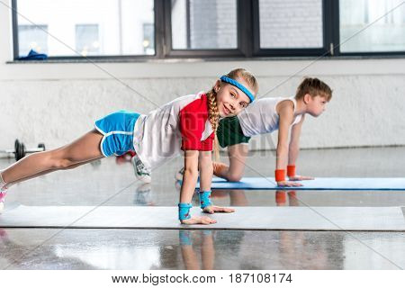 Side View Of Sporty Boy And Girl In Sportswear Doing Push Ups In Gym, Children Sport School Concept