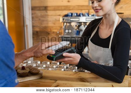 Close up of man making payment on credit card reader machine at cafe shop