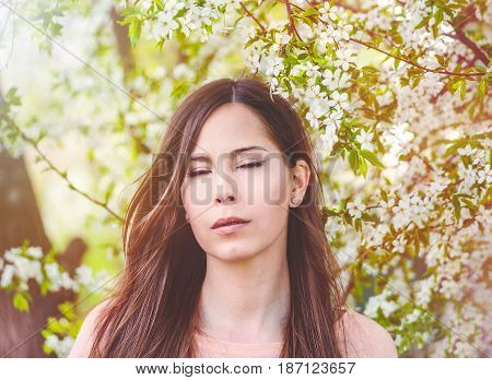 Romantic girl closeup face with close eyes, cherry blossom on the background. Pretty young woman dreaming about something closing eyes, spring time, sinny day.