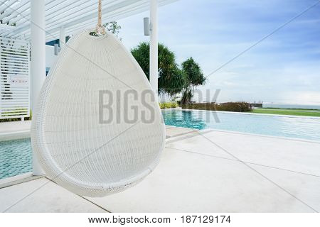 Relaxing white rattan hanging chair at swimming pool on sea view for vacation summer and travel concept.