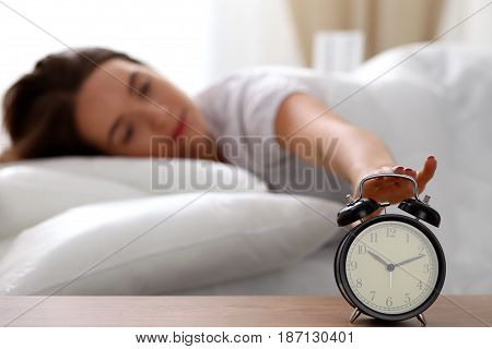 Sleepy young woman stretching hand to ringing alarm willing turn it off. Early wake up, not getting enough sleep, getting work concept