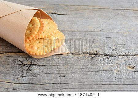 Dry salty crackers in a wrapping paper on a vintage wooden background with copy space for text. Delicious savory crackers snack idea for kids or adults