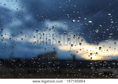 Windows with raindrops, in front of a cloudy sunset.