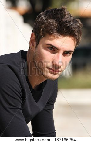 Handsome young man outdoors. Fashionable hairstyle. Black long sleeved shirt. Blurred background. The gorgeous guy has a confident and pensive attitude.