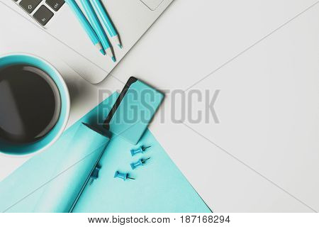 Top view of white workspace with coffee/tea mug blue supplies laptop and copy space