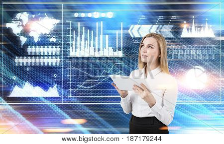 Portrait of a young blond businesswoman holding a tablet and standing near graphs drawn on blurred background.  Toned image