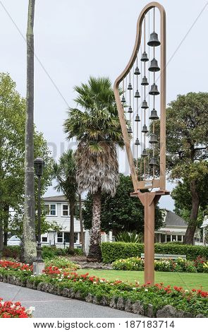 Napier New Zealand - March 9 2017: The city Carillon stands in the park of Clive Square. Created in the shape of a harp under silver sky. Green vegetation and mainly red flowers.