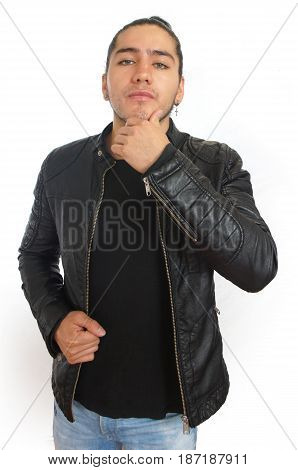 Young hispanic man with gathered hair done bow in black t-shirt and black leather jacket, with one hand on his jaw and thoughtful attitude, with the look towards the camera