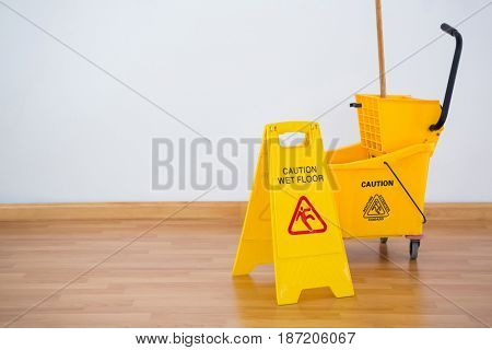 Yellow sigh boad with mop bucket on hardwood floor against wall