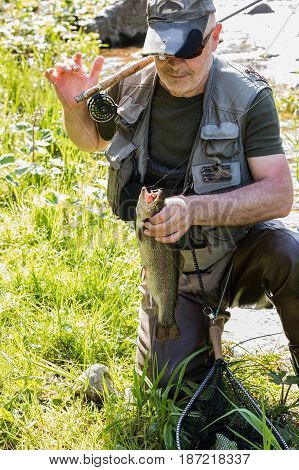 The fisherman holds the caught trout in his hand. Beautiful sunny day on the river Otava South Bohemia Czech republic.