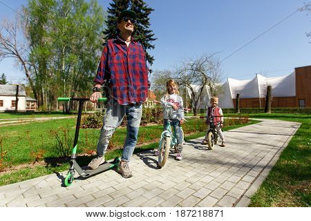 Dad with children on scooters in park during day
