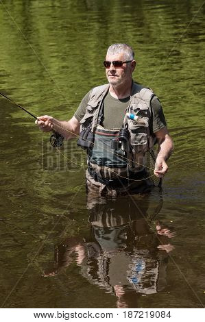 A fisherman with a pole hunts trout. A handsome man flying on the river Otava South Bohemia Czech republic.