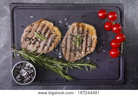 Top view of two grilled beef medallion steaks on a black wooden background