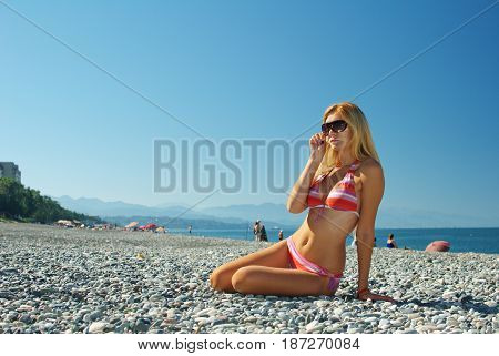 Young beautiful girl in swimsuit posing as model on beach of pebbles by the sea