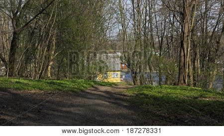 A path in the park leading to the house of yellow color standing on the shore of the lake