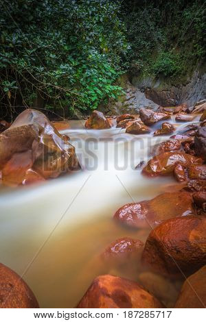 Orange volcanic river in Costa Rica cloud forest with green trees and orange rocks