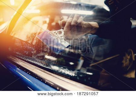 Master installs a tint film for the car glass with a hairdryer and spatula with glare of light. Concept tinting car