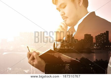 Businessman looking memo and Thinking for idea,Double exposure, panoramic view contemporary megalopolis background, orange sun light