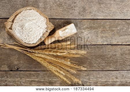 wholegrain flour in burlap bag and wheat ears on wooden table. Top view. Copy space. Baking background. Flour