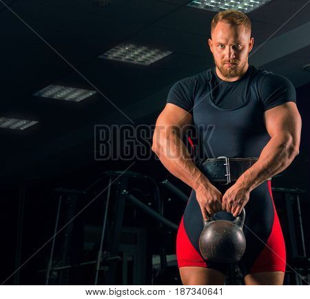 Handsome athlete stands with a weight in his hands in the gym