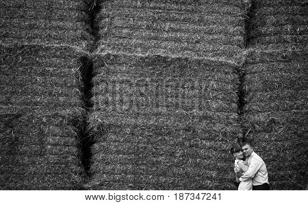 Black And White Picture Of Stunning Couple Hugging Behind A Wall Of Haycocks