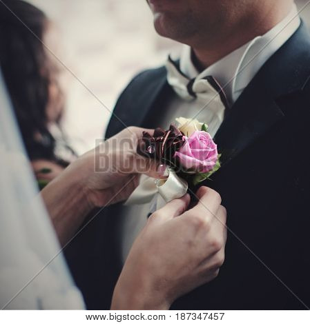 Delicte bride's hands pin pink and violet boutonniere to groom's tuxedo