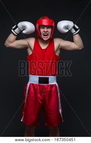 Teenage boxer in red form and white boxing gloves with hands up. Young champion. Studio shot on black background.