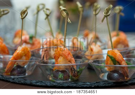 Shrimp with grapes on skewers in a transparent plate