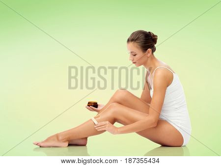 beauty, hair removal and people concept - beautiful woman with applicator applying depilatory wax to her leg over green background